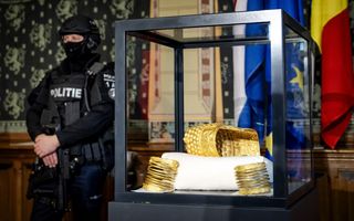 Gouden helm en armbanden in een vitrine. Ernaast een zwaarbewapende agent.