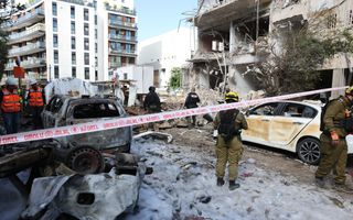 Witte, deels verwoeste woongebouwen in een stadswijk. Ook zijn auto’s verwoest. Diverse mensen zijn bezig hulp te bieden.