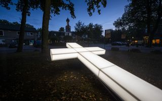 Een groot, verlicht wit kruis, tegen de achtergrond van een donker Dwingeloo.