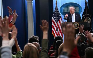 Een man staat achter een spreekgestoelte terwijl mensen in de zaal hun hand opsteken.