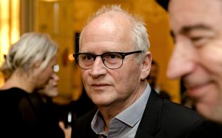 Een kalende man met een zwarte bril kijkt net niet in de camera.