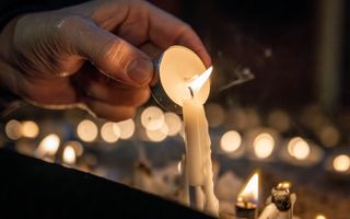 Een hand met een waxinelichtje bij een brandende kaars.
