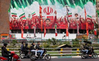 Mannen op motorfietsen rijden langs banner waarop mensen met vlaggen die hun handen in de lucht steken te zien zijn.