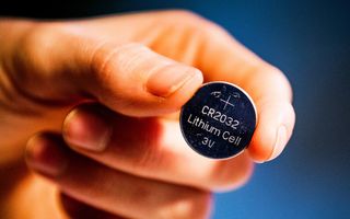 Iemand houdt een knoopcelbatterij vast.