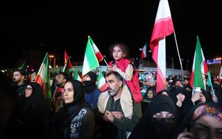 Mensen met rood-wit-groene vlaggen in de hand staan in het donker op een plein.