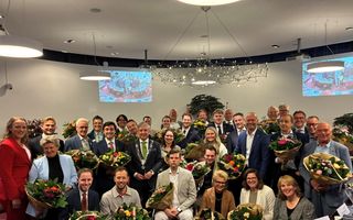 Groep mensen, netjes gekleed, met grote bossen bloemen.