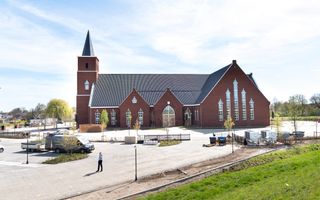 Een groot kerkgebouw met links een spitse toren. Eromheen een groot parkeerterrein waarop mensen aan het werk zijn.