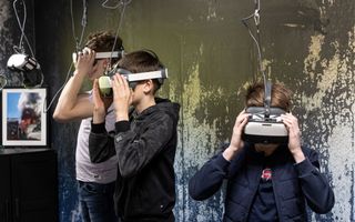Drie jongens met een VR-bril voor hun gezicht. Op de achtergrond een foto van brand in een gebouw.