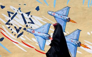 Een gesluierde vrouw loopt langs een muur waarop drie drones zijn afgebeeld. 