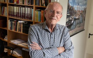 Dominee Van de Groep, een man met grijs haar, bril op, zwart-wit overhemd aan, voor een boekenkast.