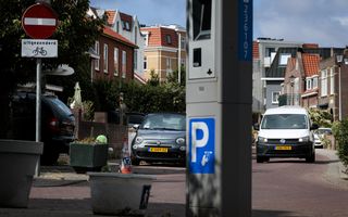 Parkeermeter met op de achtergrond een witte auto die aan komt rijden.