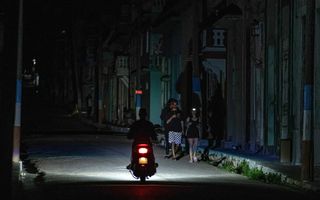 Een motor rijdt in een donkere straat. In het licht van de koplamp zijn drie mensen te zien.