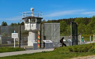 Wachttoren aan de rand van een groot hek. Op een bord staat: ”Landesgrenze”. Een root-zwart-gele paal geeft de grens tussen Oost- en West-Duitsland aan.