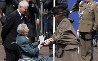 Een vrouw met een hoed overhandigt een doosje aan een man in een rolstoel.