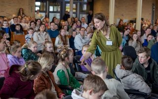 Een vrouw, met een groene jurk en een microfoon, tussen kinderen in een kerkzaal.
