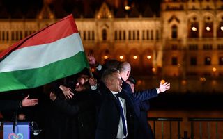 In het donker zwaait een man in pak met een rood-wit-groene vlag, zijn armen gespreid. Op de achtergrond een groot verlicht gebouw.