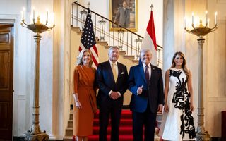 Twee mannen in blauwe pakken en twee vrouwen in fleurige jurken poseren voor een trap met een rode loper.