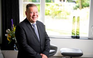 Dominee Van Estrik, een man in een donker kostuum bij een raam.