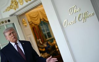 Man met grijs haar in donker pak staat voor open deur van kantoor.