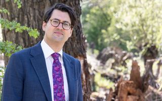 Een man in een blauw pak met een gebloemde das staat in een tuin.