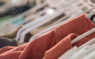 Linnen kleding van verschillende kleuren hangt op witte kledinghangers aan een rek in een winkel.