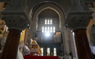Paus Leo, in gele mantel, zit op een stoel in een kerk.