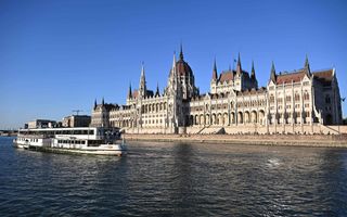 Een groot gebouw steekt af tegen de blauwe lucht. Een rondvaartboot vaart voorbij.
