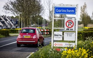 Een rode auto rijdt langs het plaatsnaambord de bebouwde kom van de stad Gorinchem binnen. 