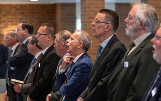 Mannen in donkere pakken staan naast elkaar en zingen.