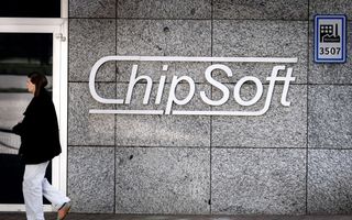 Een jonge vrouw met een zwarte jas loopt langs een grijs gebouw met daarop het logo van ChipSoft.