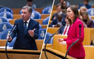 Een man en een  vrouw staan achter een zwarte microfoon. De man draagt een donker pak. De vrouw draagt een roze blazer.