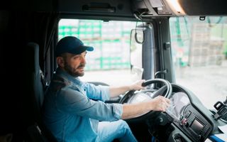 Een vrachtwagenchauffeur van middelbare leeftijd zit in de cabine van zijn vrachtwagen en vervoert goederen naar hun bestemming.
