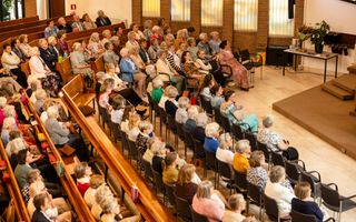Een kerkzaal vol vrouwen op banken en stoelen.