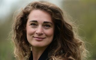 Vrouw met bruin, golvend haar kijkt in de camera.