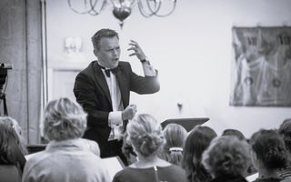 Een dirigent staat voor een koor en geeft met armgebaren aan hoe de muziek moet klinken.