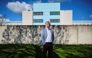 Oudere man met blauw colbert staat voor een gevangenis