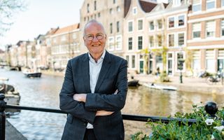 Man in pak met bril staat voor gracht.