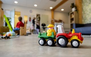 Zaal voor kinderopvang, met op de voorgrond een speelgoedtrekker. Op de achtergrond zijn vaag enkele kinderen te zien.