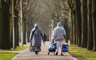 Twee mensen met hoofdbedekking dragen tassen en wandelen over een pad