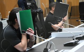Twee mannen zitten in een rechtbank en houden boeken voor hun gezicht. 