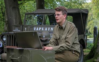 Jongeman in legeruniform speelt op groen kistorgeltje en zingt erbij.