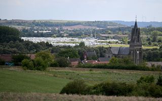 Achter een kerktoren zijn caravans zichtbaar die op een grasveld staan. 