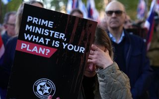 Een vrouw houdt een bord in de lucht met de tekst: ”Premier, wat is uw plan?”