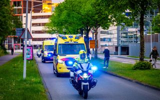 Een motoragent en ambulances met zwaailichten aan rijden over een weg.