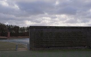 Een donker monument met letters staat voor een meer en een wolkenlucht. 