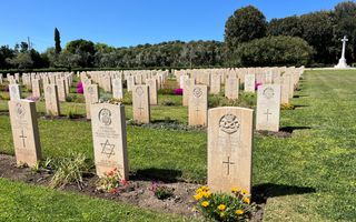 Rijen witbruine grafstenen met bloemen ervoor en gras ertussen.