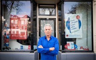 Man voor een etalageruit met blauw overhemd en grijs haar 