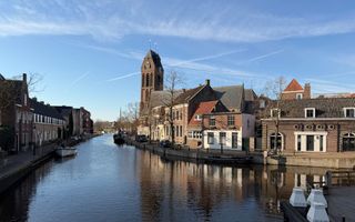 Eeuwenoude huizen staan aan het water. Op de achtergrond zijn een kerktoren en het dak van een kerk te zien.