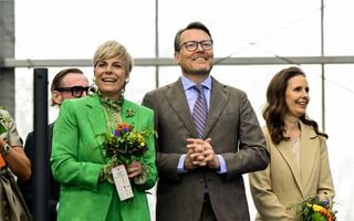 Een man in grijs kostuum en een vrouw in groene kleding lachend op de foto.