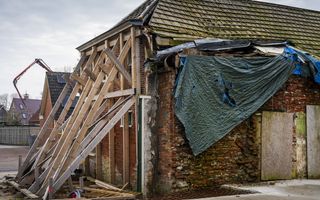 Een oude boerderij, waar aan de voorkant een houten constructie is gemaakt om het huis te versterken.
